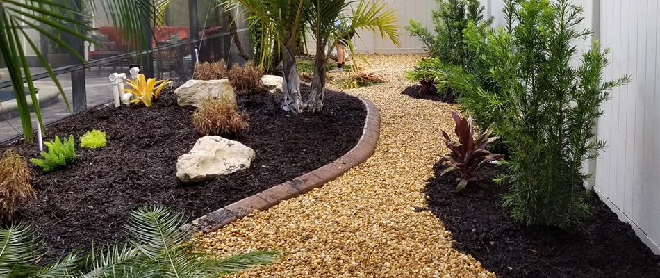 New landscaping bed installation with concrete curbing, mulch, and rock at a home in Palmetto.